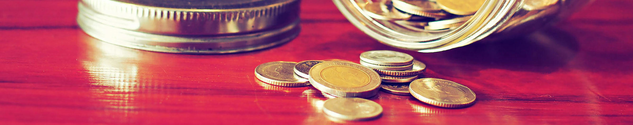 Tipped over mason jar of coins on a red surface