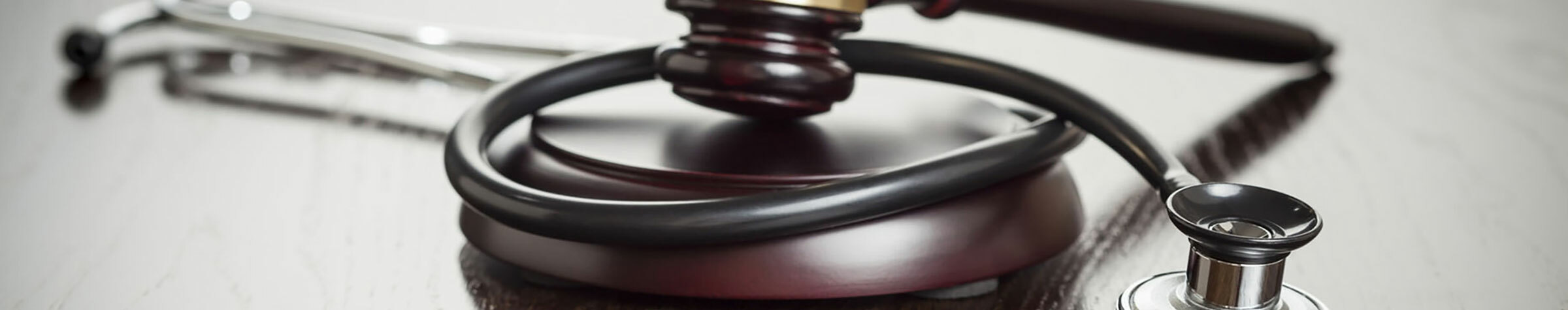 Black stethoscope wrapped around a wooden gavel and block on a wood surface