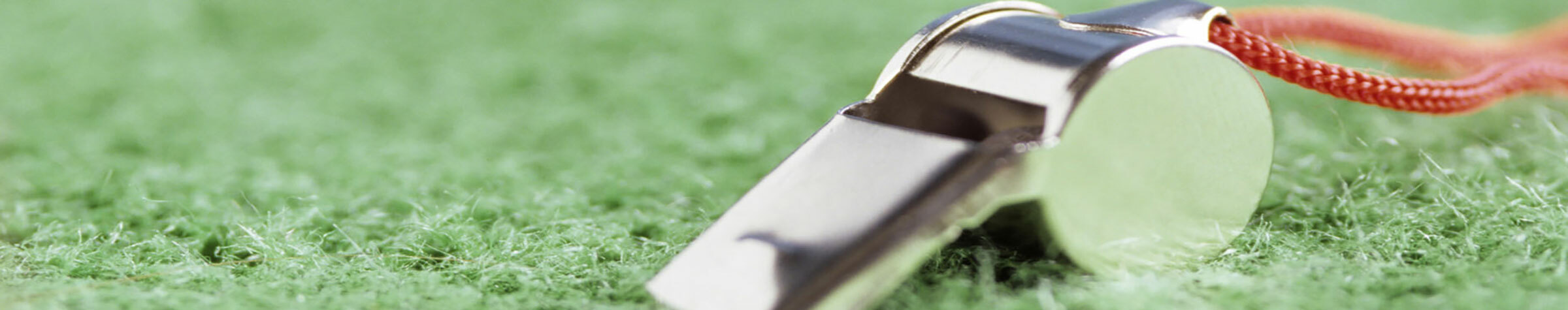 Silver whistle with a red lanyard on green turf